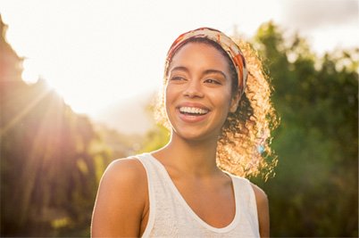 young woman smiling outside with sun shining 