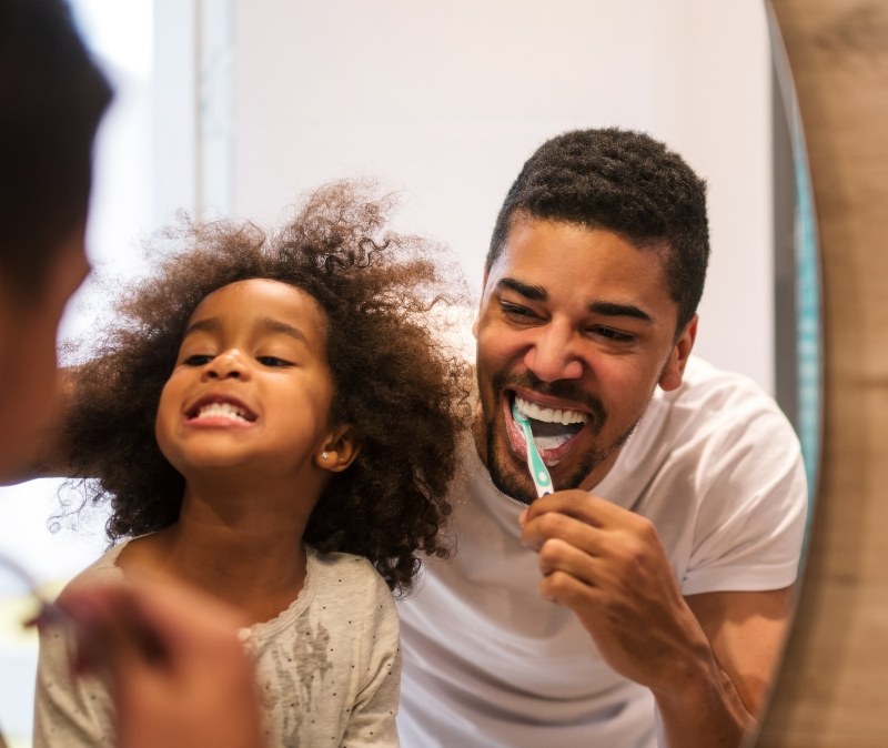 Father and daught brushing teeth together to prevent dental emergencies