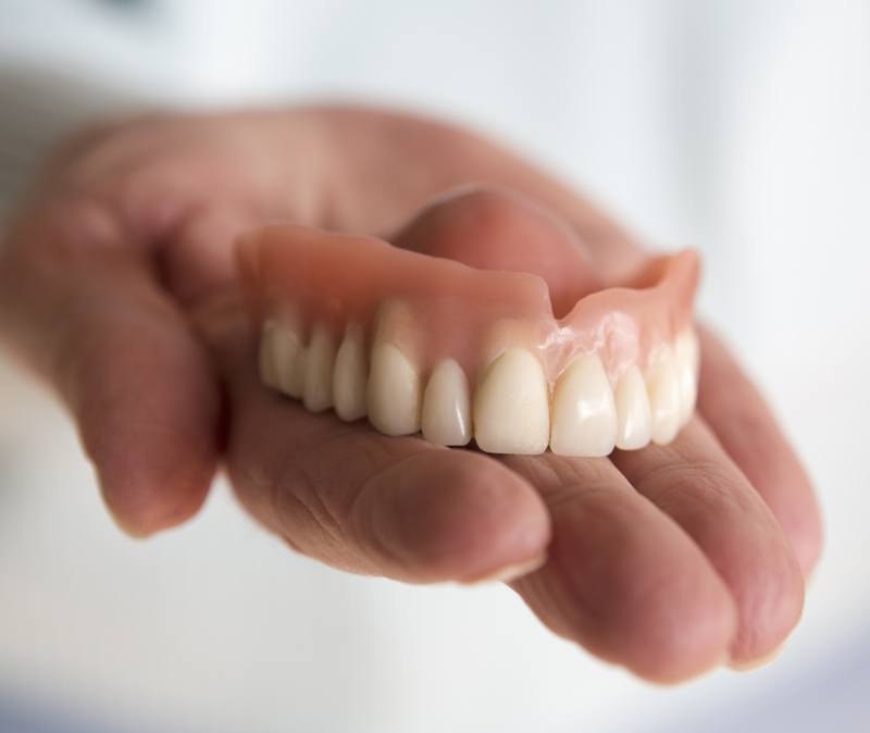 Hand holding full set of dentures