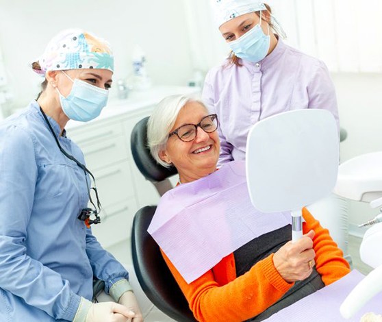 Happy senior patient looking at her smile in mirror