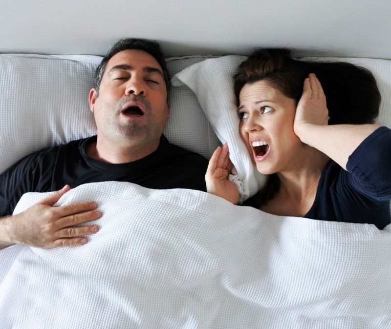 Woman frustrated in bed with snoring man in need of sleep apnea treatment