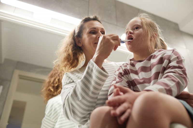 Mother helping child prevent dental emergencies by brushing their teeth